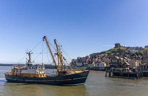 A fishing boat on water near a harbour and town on a sunny day