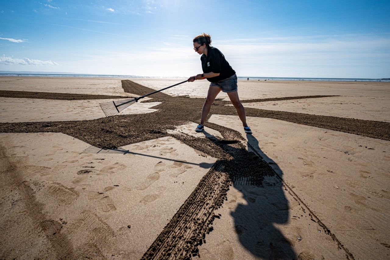 A female artist rakes sand on the beach at Saunton Sands