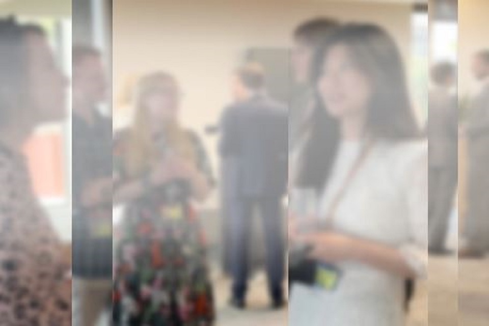 Image of people standing and chatting. The image is blurred as if it has been taken through thick glass.