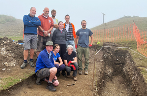 Группа мужчин и женщин, принимающих участие в археологических раскопках, позирует рядом с траншеями, вырытыми на склоне холма на побережье Дорсета.