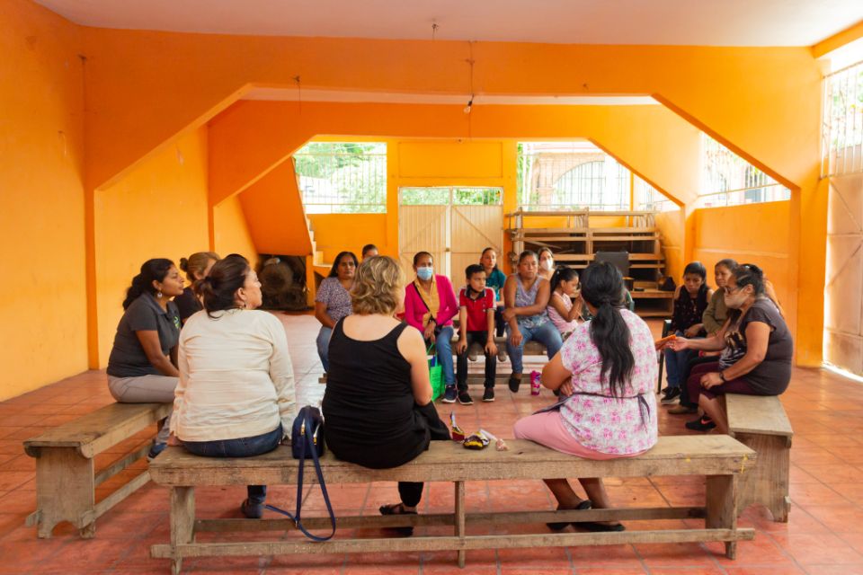 A group of people are having an informal conversation inside a rural classroom