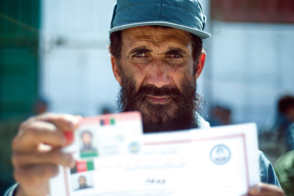 An officer from the Afghan Uniform Police proudly holds up his certificate and ID card