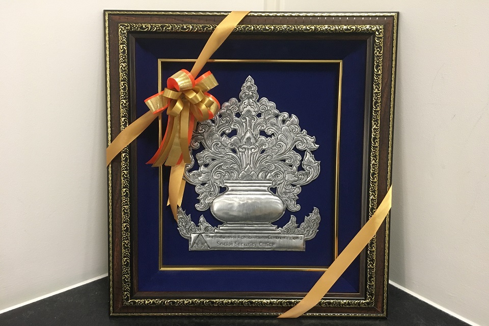Large, silver decorative plaque which is displayed with a yellow ribbon and bow wrapped around it.