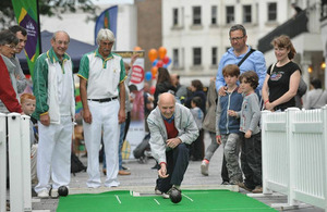 A man plays bowls while several people look on watching