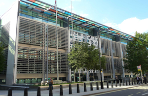 A large office building is pictured, it has multicoloured windows. Street bollards are in the foreground.