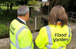 Два инспектора по наводнениям в желтых светоотражающих куртках стоят спиной к камере.