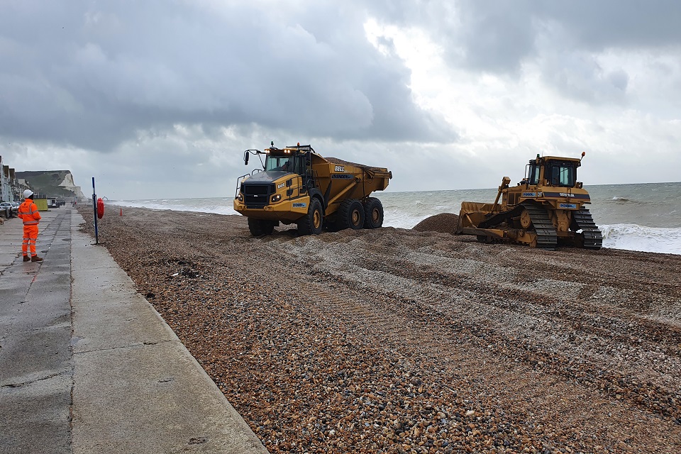 A bulldozer and a lorry are shown moving shingle around Seaford beach to retain protection froim flooding