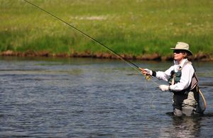 Женщина, стоящая в реке и ловящая рыбу на фоне травянистого берега