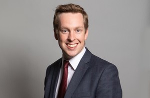 Portrait of Minister for Disabled People, Tom Pursglove he is smiling and looking directly at the camera wearing a dark suit and red tie.