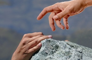 Hand reaching out to another hand on mountain.