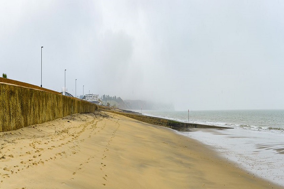 A long sandy beach at Yaverland is seen, with the sea wall on the left, and misty skies and properties in the distance 