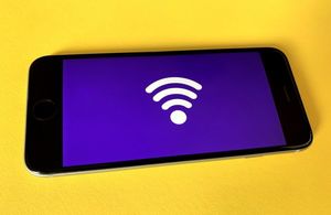 Image of a mobile phone with a purple backdrop on screen with a big wireless reception symbol on the mobile phone screen. The mobile phone is sitting on a bright yellow background.