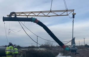 A crane lowering a pump designed to sit in water with pipework attached being lowered