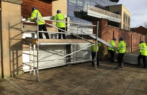 A group of men in yellow jackets can be seen on scaffolding erecting a flood barrier at Frankwell in Shrewsbury