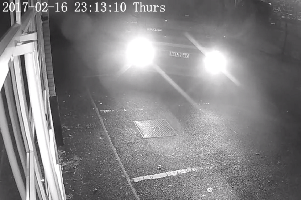 A black and white CCTV image shows the headlights of a lorry coming into view 