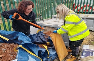 An Environment Agency officer shovels tiny pieces of rubble into a bag held by a colleague