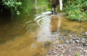 A person in wellies walks through a shallow watercourse turned yellow by all the sediment