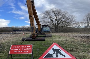 A digger in front of a sign which says 'keep clear heavy plant work'