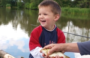 A boy holding a little fish on the lake side.