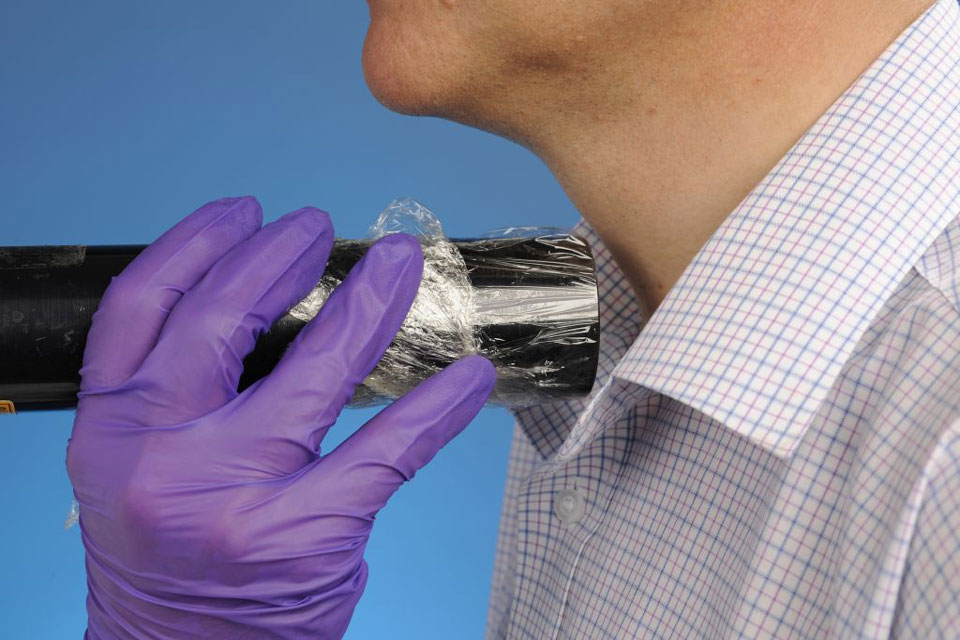 A hand wearing purple nitrile gloves holding a handheld detector close to a man's neck