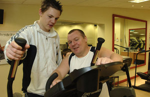 Teenage boy on a gym machine and a male trainer showing him what to do