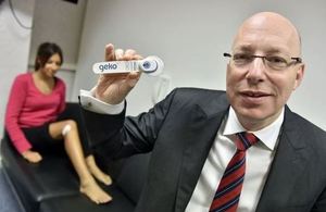 Bernard Ross, CEO of Sky Medical, holding up to camera a Geko medical device. Female patient in the background.