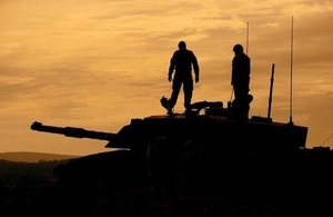 British Army reservists standing on a Challenger 2 tank, silhouetted against an orange sky