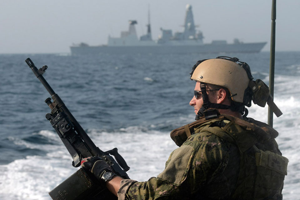 A general purpose machine gun aimer from a US Navy Riverine Command Boat deployed from RFA Cardigan Bay passes HMS Diamond