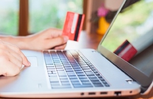 person at laptop with payment card in hand