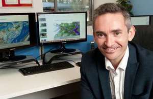 Ambiental CEO Justin Butler in his office with flood mapping imagery on screens in the background