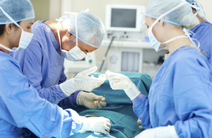 An image of surgeons wearing face-masks, hair-nets and gloves operating on a patient.