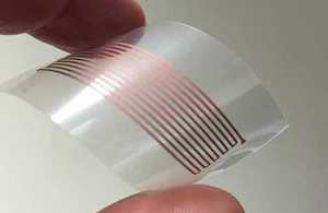 Finger tips holding a flexible, clear plastic printed with a copper-based nanoparticle conductor
