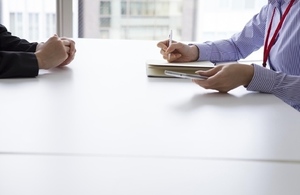 two people either side of desk with hands visible and one person taking notes