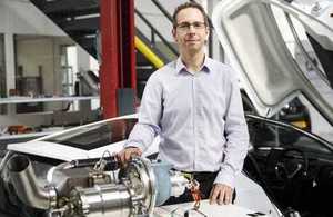 Nick Carpenter, engineering director of Delta Motorsport, pictured in factory with prototype electric car behind and a turbine device on bench in the foreground.