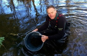 Image shows Paul Frear putting fish into the river