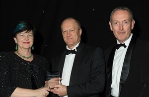 Baroness Neville-Rolfe presents the award to John Clarke with Lord Hutton in attendance