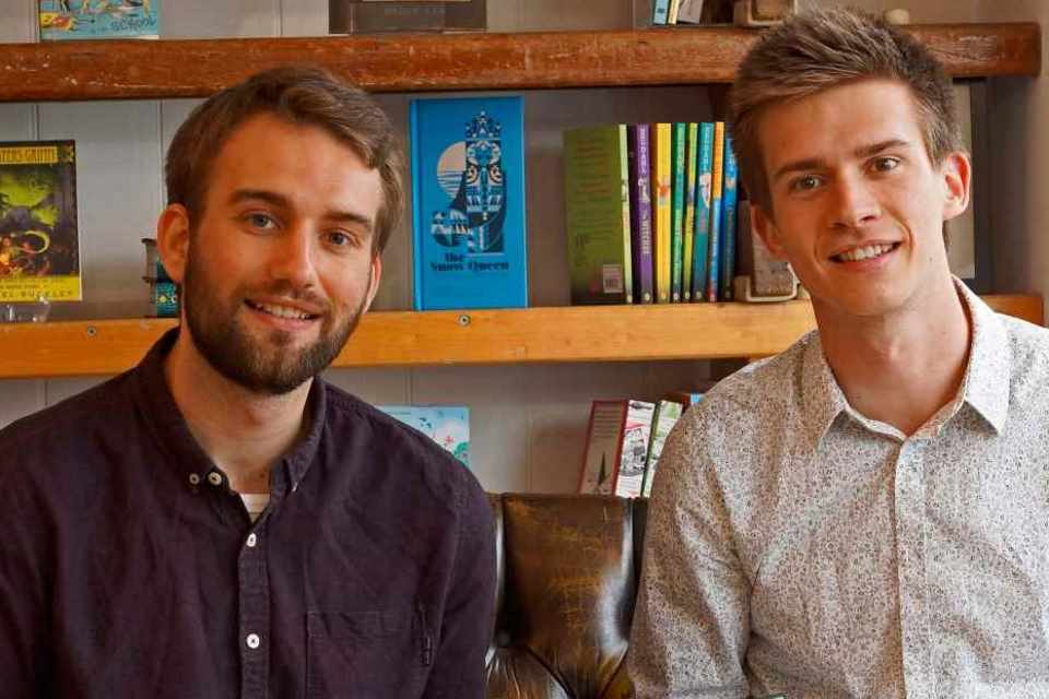 Entrepreneurs Alex Somervell and Jonny Pryn with book and bookshelf behind