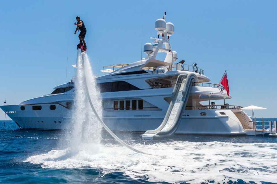 Man airborne on jet pack in front of superyacht with water slide.