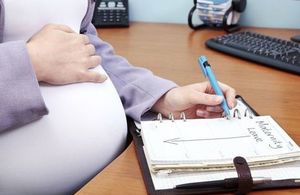 Pregnant woman in an office writing the words Maternity Leave in her diary.