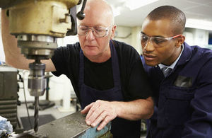 Engineering apprentice observing an older man operating machinery