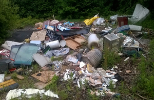 Photograph showing household waste, including a mattress and broken furniture, strewn around a woodland clearing.