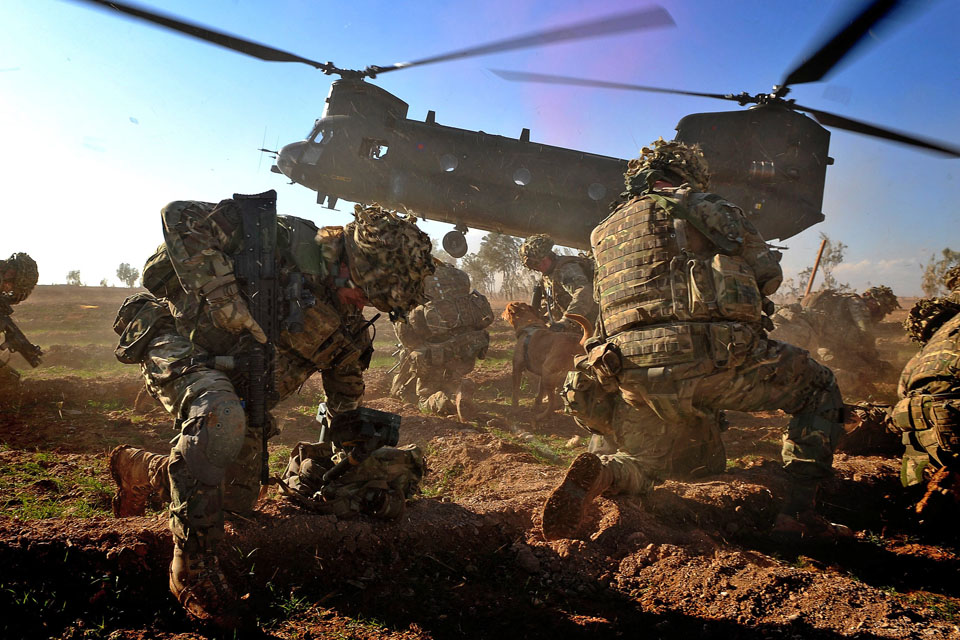 Royal Marines brace themselves against the downdraft from an incoming RAF Chinook helicopter