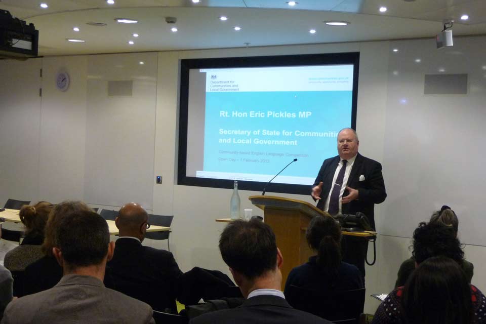 Eric Pickles giving a speech in front of a Powerpoint slide.