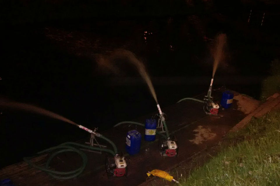 Hydrogen peroxide being sprayed into the water at night from three sprayers on the riverbank
