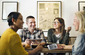 Group of 4 friends gather together around smart phone and laptop