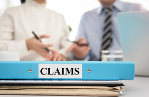 stack of papers and a claims folder with two people at desk in background