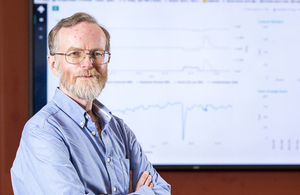 Upside Energy co-founder Graham Oakes standing with arms crossed on he left, with graph on a white board behind him.