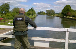 Rear view of man standing on bridge overlooking canal wearing a lifejacket with fisheries officer on back