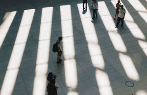 People standing in between strips of light and shadows on the ground.