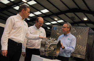 Three men in shirt sleeves in conversation over a transmission system exhibit.